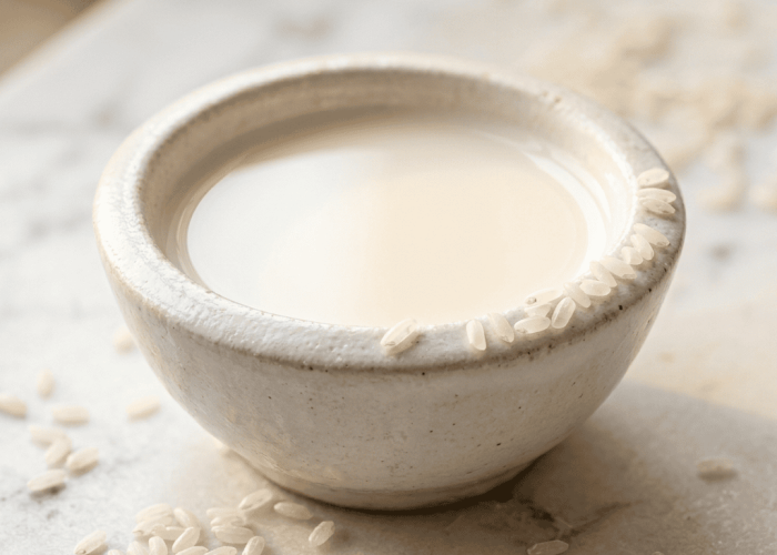 Ceramic bowl of silky white rice milk with raw rice grains on white marble surface