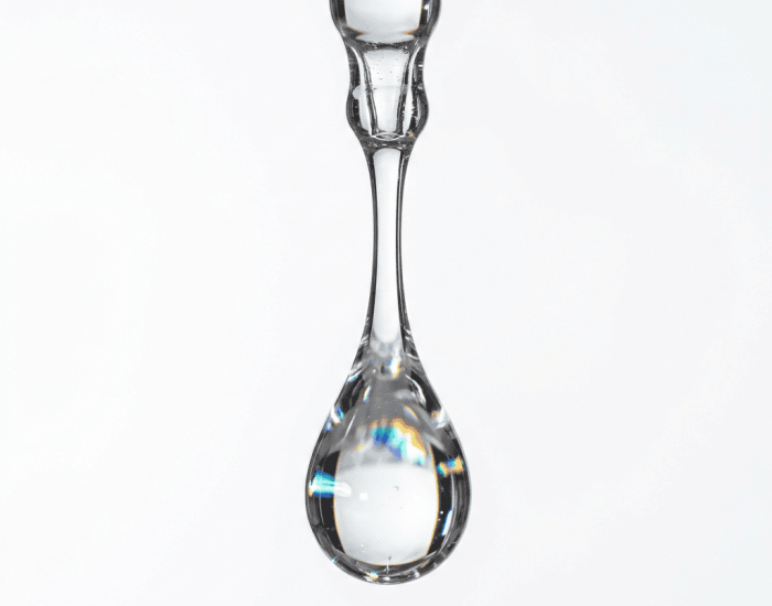 Thick clear glycerin drop suspended from glass pipette tip with rainbow refractions