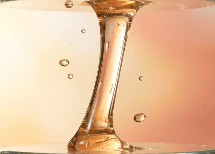 Golden panthenol liquid stretching between glass rod and surface showing viscous consistency